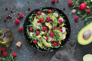 Avocado salad with raspberry, pomegranate, arugula and sesame on dark background. Top view with copy space. Healthy food. Vegetarian and vegan food.