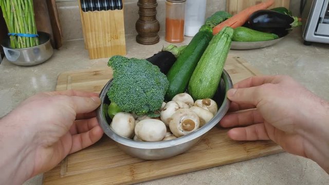 Home cooking - Small stainless steel dish of assorted vegetables like eggplant, zucchini, squash and broccoli with mushrooms. More vegetables in background like carrots and asparagus.