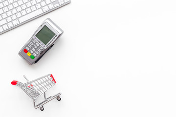 making purchase online with card machine, keyboard and mini trolley on white desk background top...