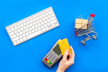 making purchase online with card machine, card, keyboard and mini trolley on blue desk background...