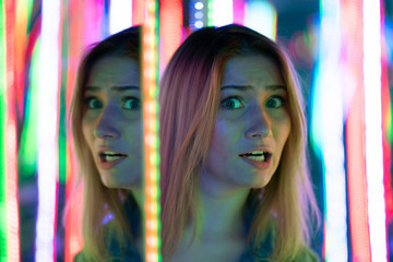 Obraz premium sweet caucasian girl walks in a mirror maze with colorful diodes and enjoys an unusual attraction room in the city