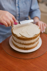 The confectioner levels the cream on the cake. The cook creates a cake, collects it and covers it with cream and then levels it with a spatula and a scraper.