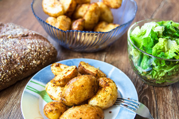 Baked young potatoes on a plate, homemade whole grain bread and lettuce salad on vintage wooden table