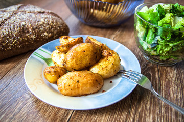 Baked young potatoes on a plate, homemade whole grain bread and lettuce salad on vintage wooden table
