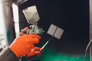 Car repair service. Worker painter checking color matching before painting. spraying black liquid...