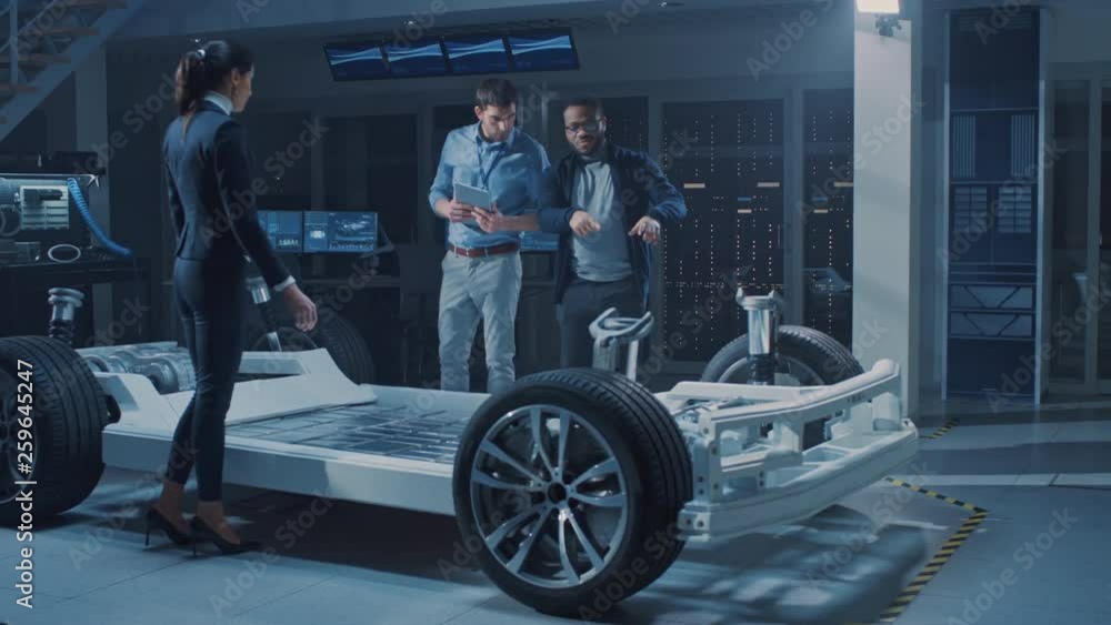Poster female project manager talks about electric car prototype with her team of engineers, showing chassi