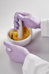 Closeup of the hands of a pharmacist or scientist, holding a mortar and pestle and wearing rubber gloves,pharmacist mixing medicine