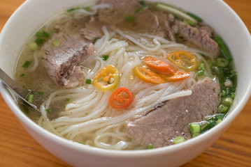 Beef soup pho close up, in a budget restaurant in Ho Chi Minh City, Vietnam for 45 000 dongs (2 US dollars). Noodles and sliced boiled meat with chili and chopped spring onions in broth.