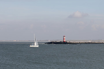 view of lighthouse on stones near sea with yacht