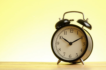 Black alarm clock on the wooden surface against the yellow background.