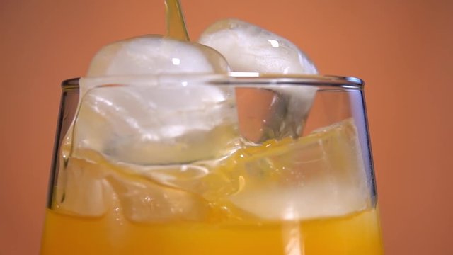 Yellow lemonade pouring in the glass with ice cubes from the jug. Orange or pineapple juice. Making bubbles. Slow motion.