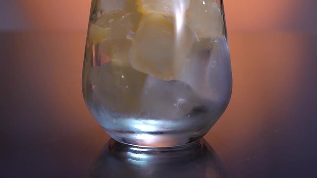 Yellow lemonade pouring in the glass with ice cubes from the jug. Orange or pineapple juice. Making bubbles. Slow motion.