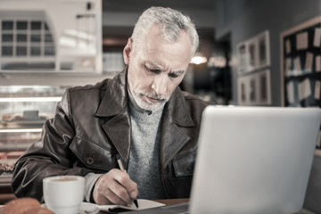 Concentrated gray-haired male making notes in copybook