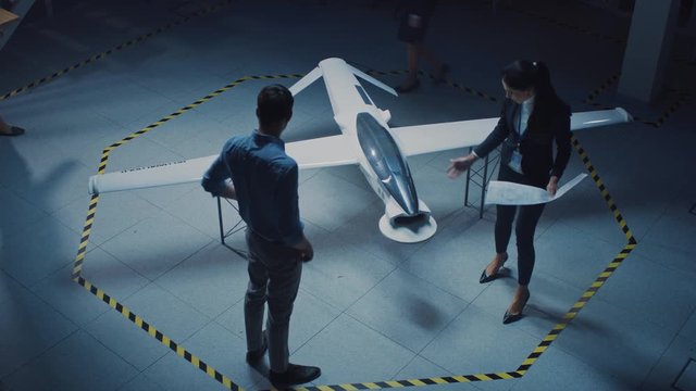 Meeting of Aerospace Engineers Work On Unmanned Aerial Vehicle / Drone Prototype. Aviation Experts in White Coats Talking. Industrial Laboratory with Surveillance or Military Aircraft. Elevated Shot