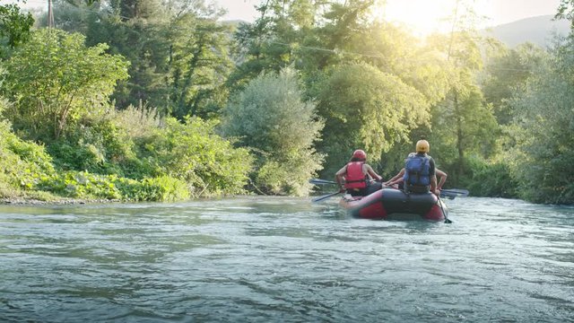 Group of people on raft boat doing rafting on river during sunset or sunrise. Warm back light. Friends italian trip in Umbria.4k slow motion