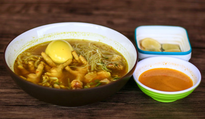 Soto ceker or chicken feet soup, chili sauce and lime on wood background. 