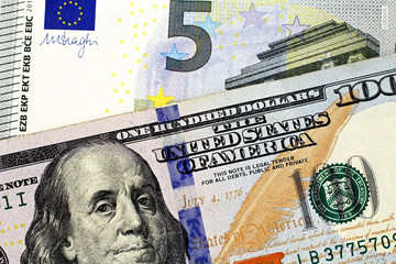 A close up image of a European Union five Euro note with an American one hundred dollar bill in macro