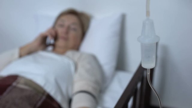Aged female patient talking phone in sickbed, suddenly feeling strong headache