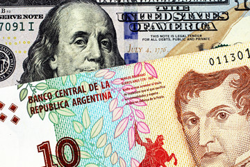 A close up image of a blue, new American one hundred dollar bill close up with an Argentinian ten peso bank note in macro
