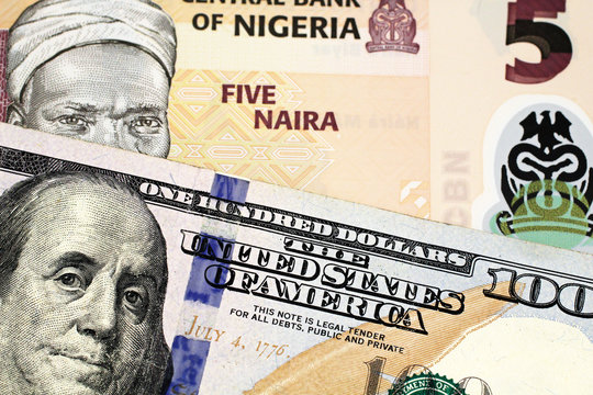 A macro image of a peach colored Nigerian five Naira bill with an American one hundred dollar bill close up