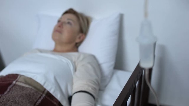 Sad aged patient lying in sickbed under dropper, patient-controlled analgesia