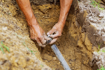 Man Working with Pipes in Ground while Installing a New Underground Sprinkler System - obrazy, fototapety, plakaty