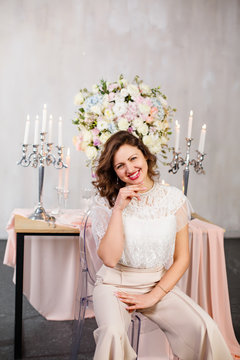 Young woman near decorated table. with flowers. Brunettee woman in her wedding day. Sexy young beautiful woman in elegant pantsuit. Luxurious woman in a beautiful lace suit. Pink decore