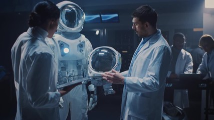 Diverse Team of Aerospace Scientists and Engineers Wearing White Coats have Discussion, Use Computers, Construct Astronaut Helmet for New Space Suit Adapted for Galaxy Exploration and Travel.