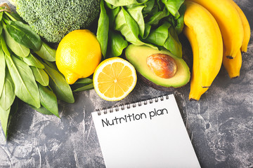 Nutrition plan concept. Greens, spinach, avocado, banana and lemon on moody background. Healthy eating, diet and vegetarian. Horizontal shot. Copy space for your text.