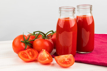 Two Bottles of Tomato Juice with Fresh Ripe Tomatoes on a light wooden table.