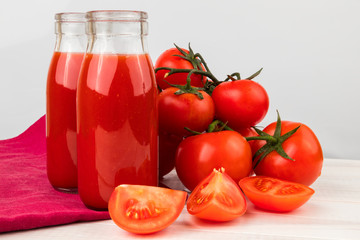 Two Bottles of Tomato Juice with Fresh Ripe Tomatoes on a light wooden table.