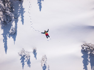 Winter aerial view portrait of Snowboarder female lying in clean snow between Christmas trees. Snowy mountain in ski resort, sunny winter holiday