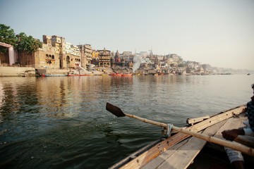 Fototapeta na wymiar Ganga river and Varanasi ghats morning view with buildings from river and boat. Smoke from bonfires