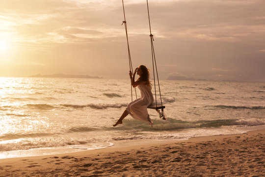 Silhouette of woman on swing above sea shore on sunset