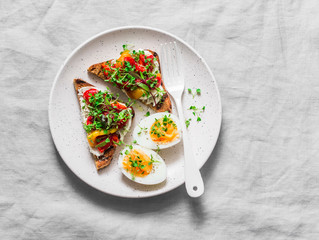 Healthy breakfast or snack - whole grain bread, feta, pickled pepper sandwiches and boiled egg on gray background, top view
