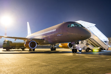 White passenger jet plane with boarding steps at the night airport apron