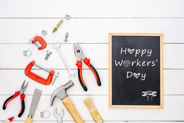 Happy Workers' Day background concept. Flat lay of construction handy tools with black chalkboard with Happy Workers' Day text over white wooden floor background.