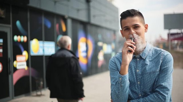 stylish young man vaping near the supermarket on the street