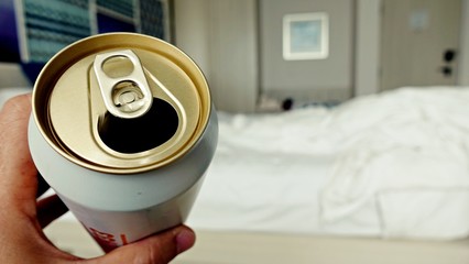 Man sitting in the bedroom and drinking a cold beer after work in the evening. Hand holding a aluminum can.