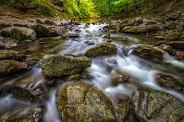 Naklejka na ściany i meble Scenic view of amazing water motion blur of a water stream between rocks.