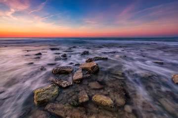 Beautiful rocky beach with stones in blurred water, the colorful sky at sunrise. Black sea, Bulgaria. Landscape with the sea waves and rocks.