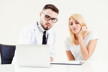 Male doctor talks to female patient in hospital office while looking at the patients health data on...