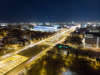 Fototapeta na wymiar Night cityscape of soccer stadium and highway with trails of cars captured with long exposure. UAV drone aerial view