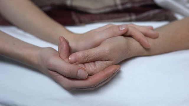 Warm daughters hands stroking and calming down sick mother in bed, assistance