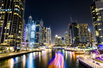 Fototapeta na wymiar Stunning view of the Dubai Marina at dusk with illuminated skyscrapers in the background and a light trails left by a yacht sailing in the foreground. Dubai, United Arab, Emirates.