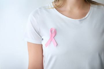 Woman with pink ribbon on white background, closeup. Breast cancer awareness concept