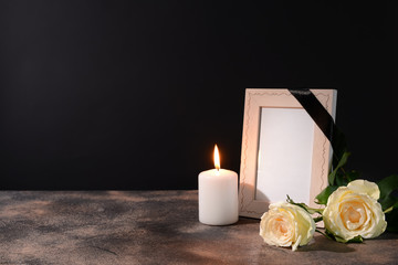 Blank funeral frame, candle and flowers on table against black background