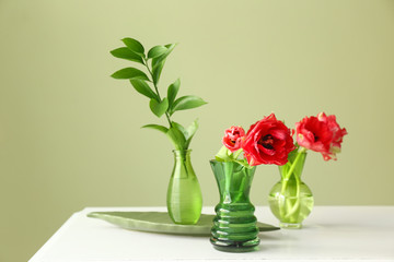 Vases with beautiful flowers on table against color background