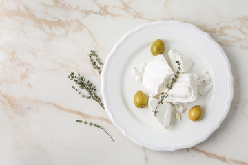Plate with tasty feta cheese, thyme and olives on light table