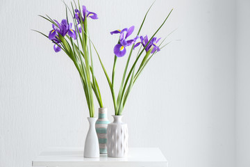 Vases with beautiful flowers on table against white background
